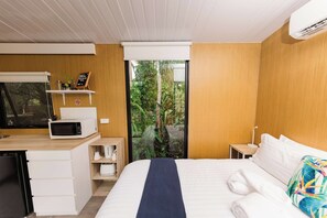 A hotel room with a bed, a desk with a microwave, a small coffee maker, and a view of greenery outside. - The Stables by Tiny Away (Palmwoods)
