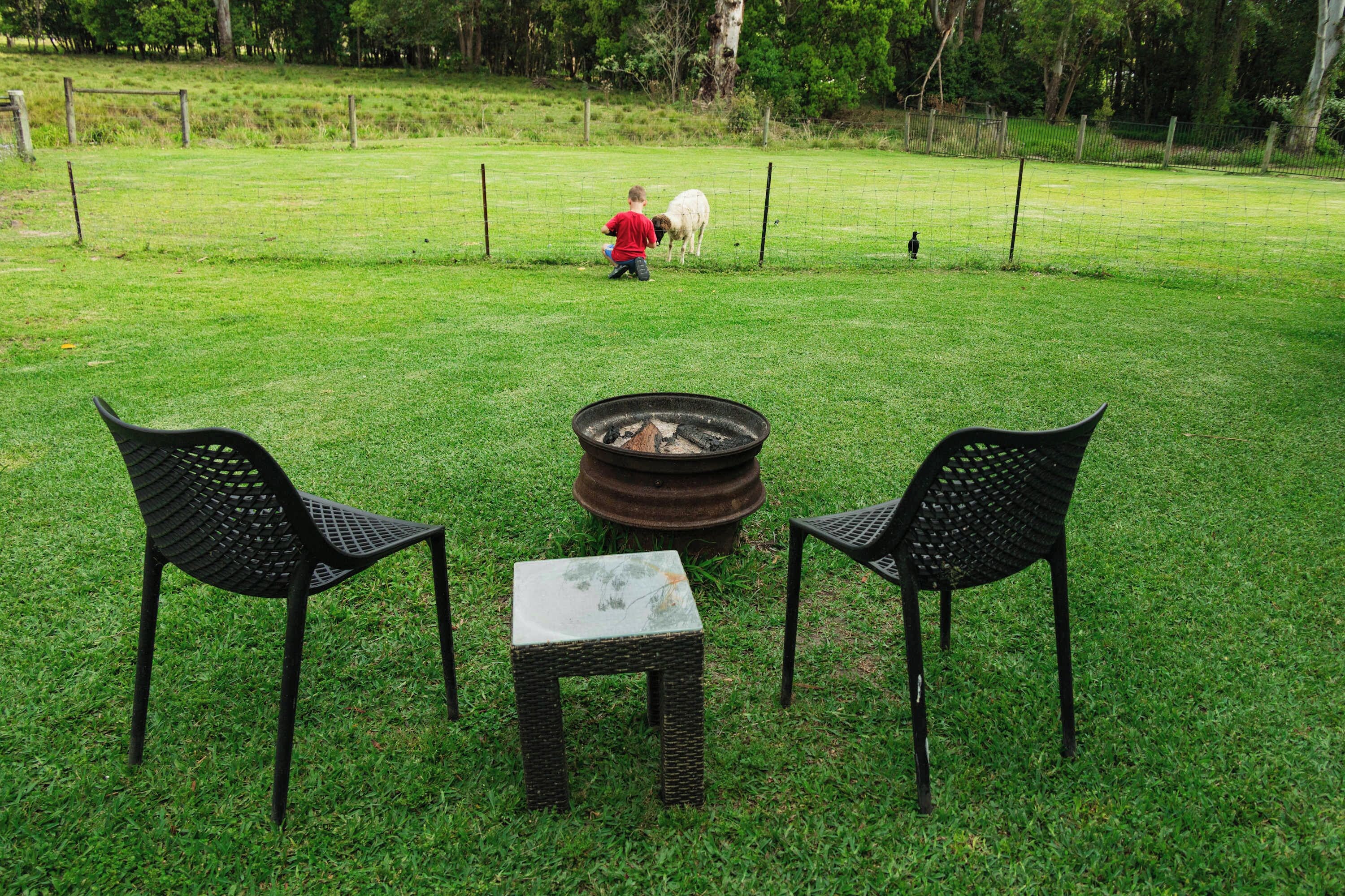 A grassy outdoor area with a fire pit, two chairs, and a table.