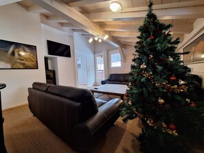 Sala de estar com um sofá de couro escuro, uma mesa de centro e um pinheiro de Natal com enfeites.