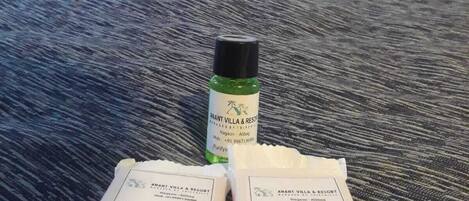 A hotel room with a bed, pillows, and a table with a bottle and two packets of Revitalizing Bath Soap.