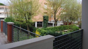 Ein Balkon mit Blick auf ein Gebäude mit rosa Fassade, umgeben von Grünpflanzen und einem Metallgeländer.