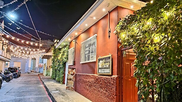Una calle estrecha bordeada de edificios, uno de los cuales muestra un letrero que indica un restaurante.
