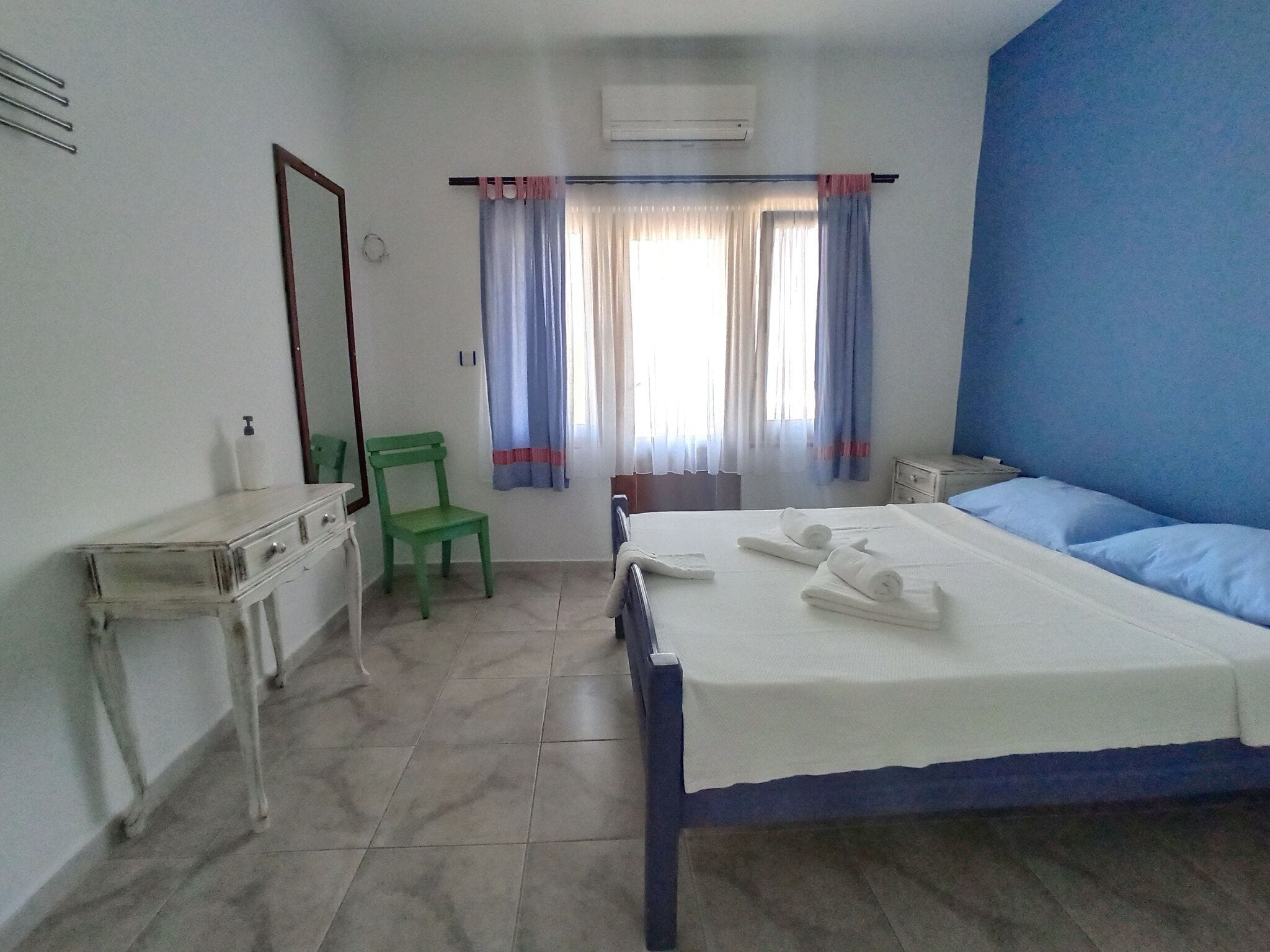 A bedroom with a bed, a chair, a desk, a mirror, and curtains.