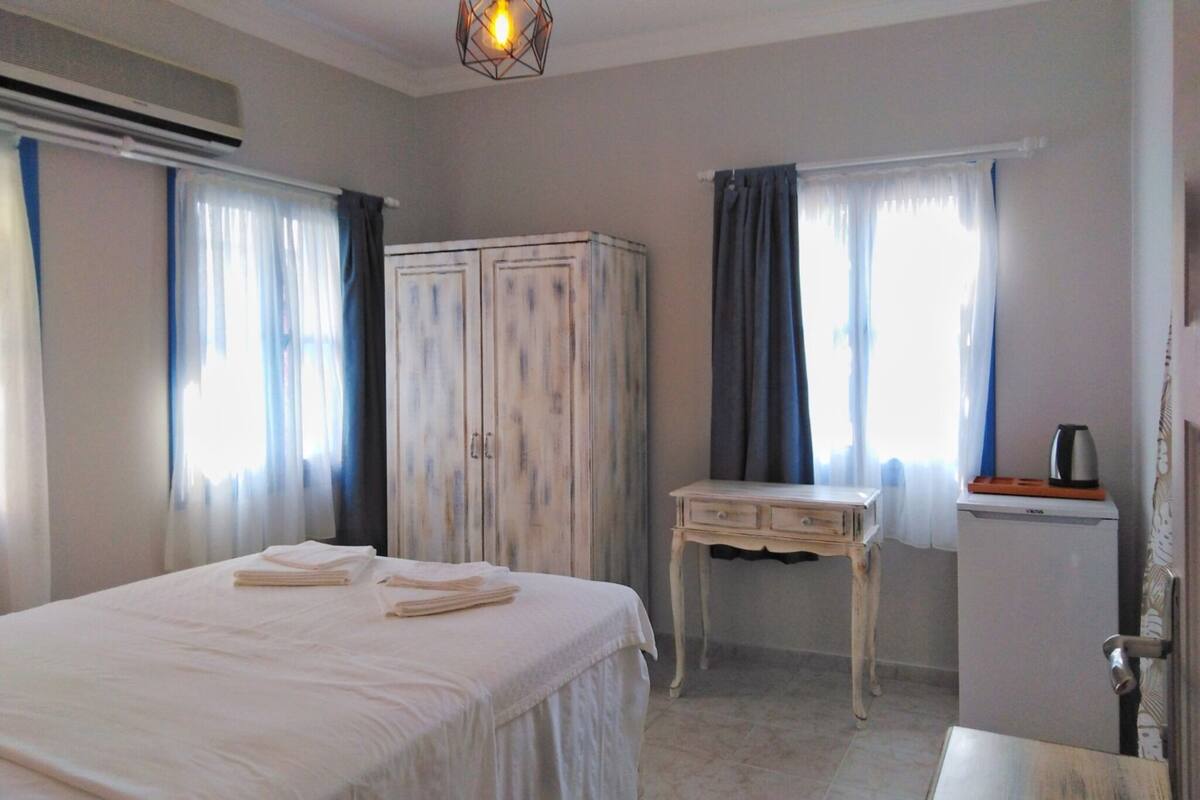 A bedroom with a bed, a wardrobe, a desk, and a kettle.
