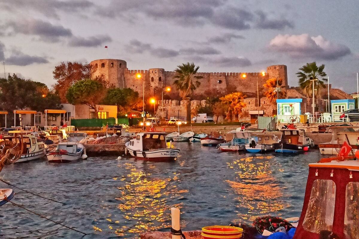 A harbor with boats docked, a castle in the background, and a clear sky.