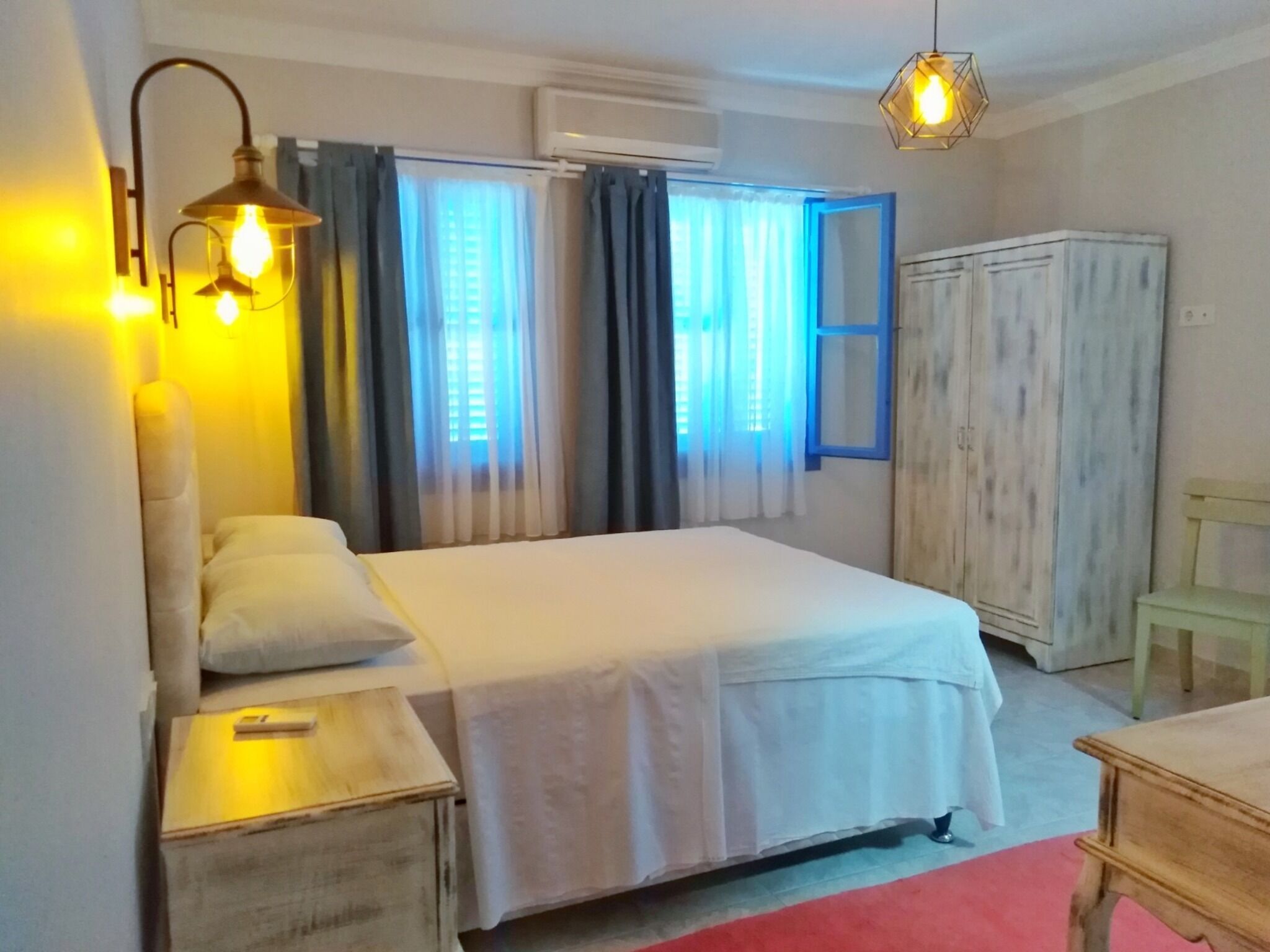 A bedroom with a bed, bedside table, lamp, wardrobe, and curtains.