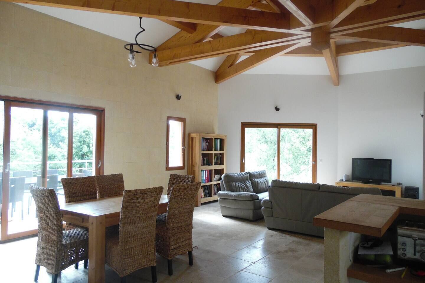 A spacious living area with a dining table, chairs, a sofa, a bookshelf, and a television.