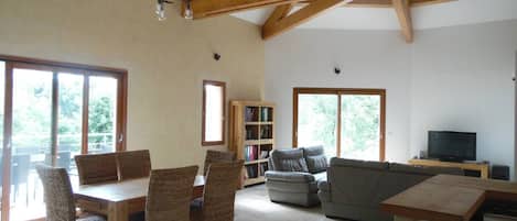 A spacious living area with a dining table, chairs, a sofa, a bookshelf, and a television.