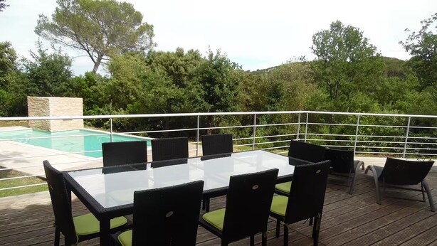 Mesa con cubierta de vidrio, sillas negras y una piscina al fondo.