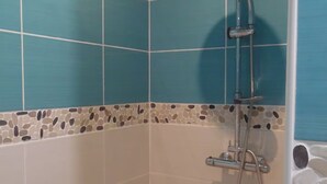 Un baño con azulejos azules, una ducha con cabezal de ducha manual y suelo de baldosas.