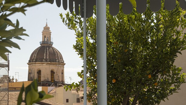 A balcony with a view of a dome building, a tree with oranges, and striped cushions.
