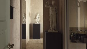 A hallway with a statue, a mirror, and a door.