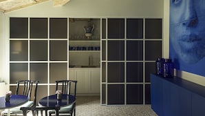 A room with a large window, a dining area with two chairs and a table, and a wall with a large blue painting.