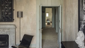 A room with a fireplace, a chair, a sculpture, and a hallway leading to another room.