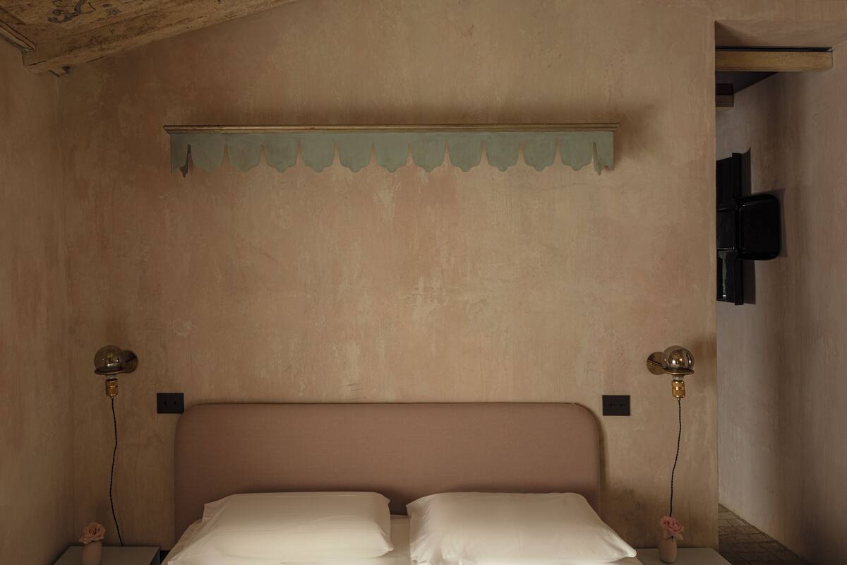 Une chambre à coucher avec un lit, deux lampes de chevet, un téléviseur fixé au mur et un objet décoratif sur la table de chevet.