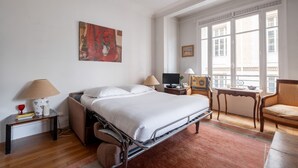 A hotel room with a bed, bedside tables, a chair, a window, and artwork on the wall. - Flowers from Paris, by Veeve (Paris)