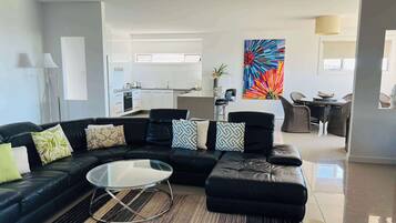 A modern living room with a black leather sectional sofa, a glass coffee table, and a vibrant abstract painting.
