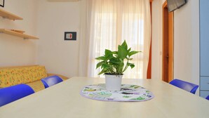 A dining area with a table, chairs, a potted plant, a sofa, and a TV mounted on the wall.