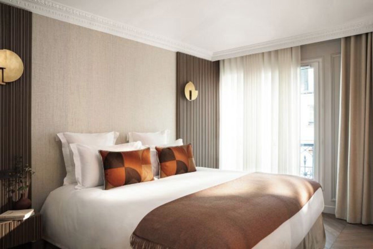 A hotel room with a large bed, a bedside table, a wall clock, and a window with curtains.