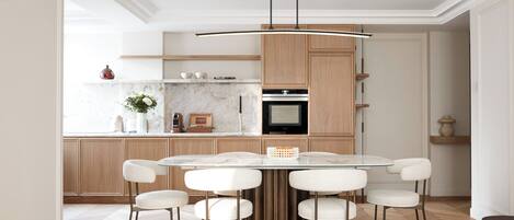 A modern kitchen with a marble countertop, wooden cabinets, and a central island with chairs.