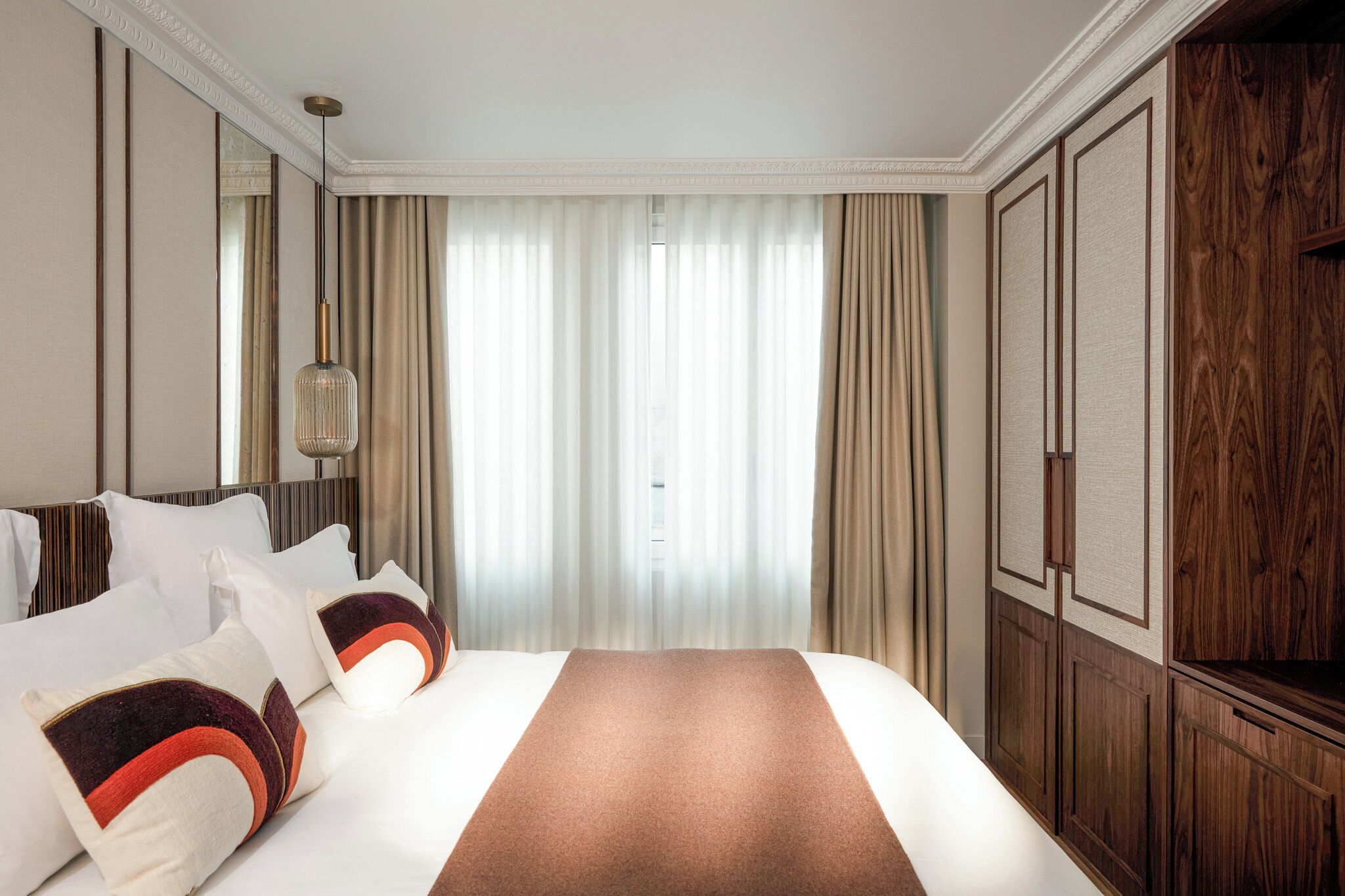 A hotel room with a large bed, a wooden wardrobe, and a mirror on the wall.