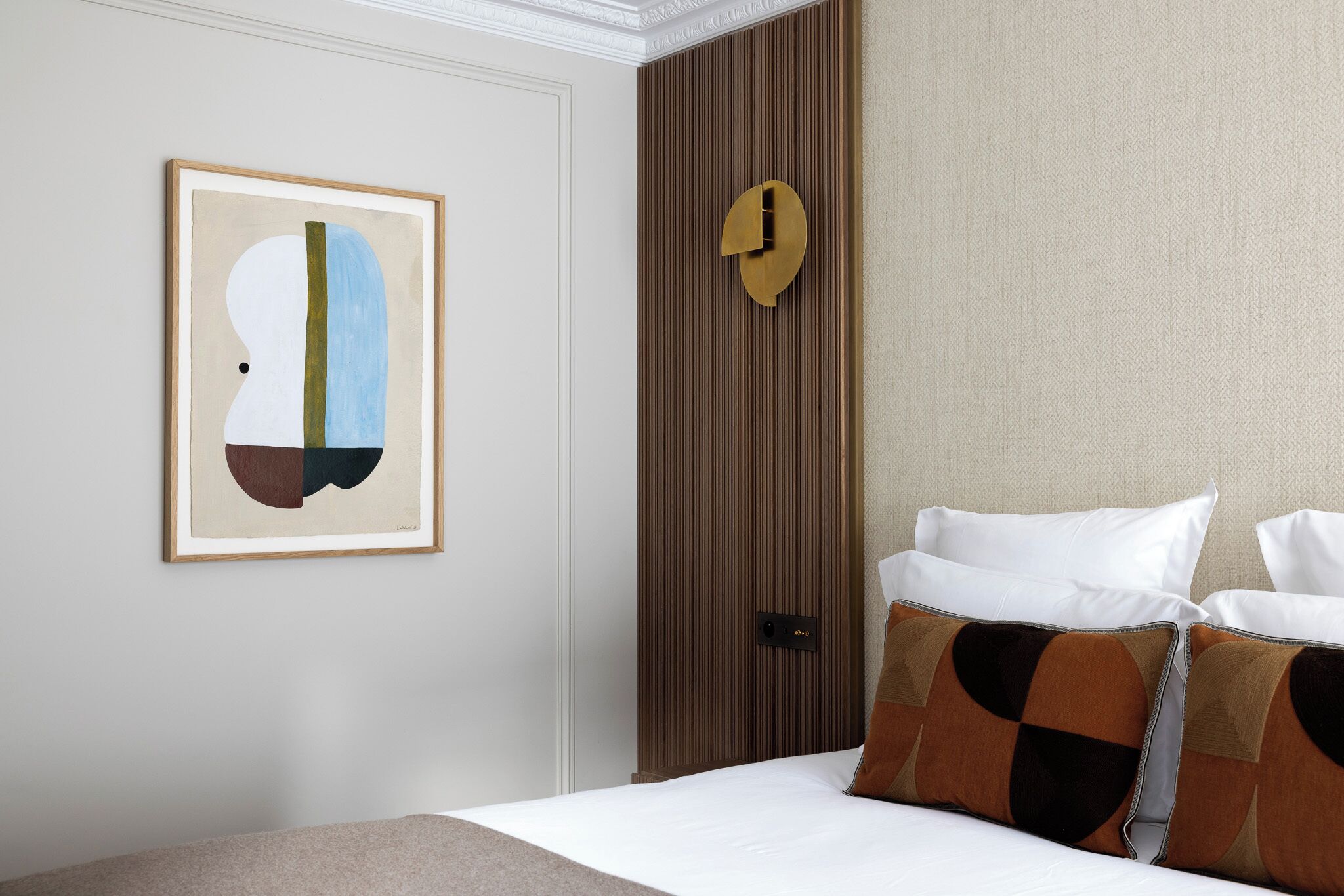 A hotel room with a bed, a framed abstract painting, a wall clock, and a textured wall panel.