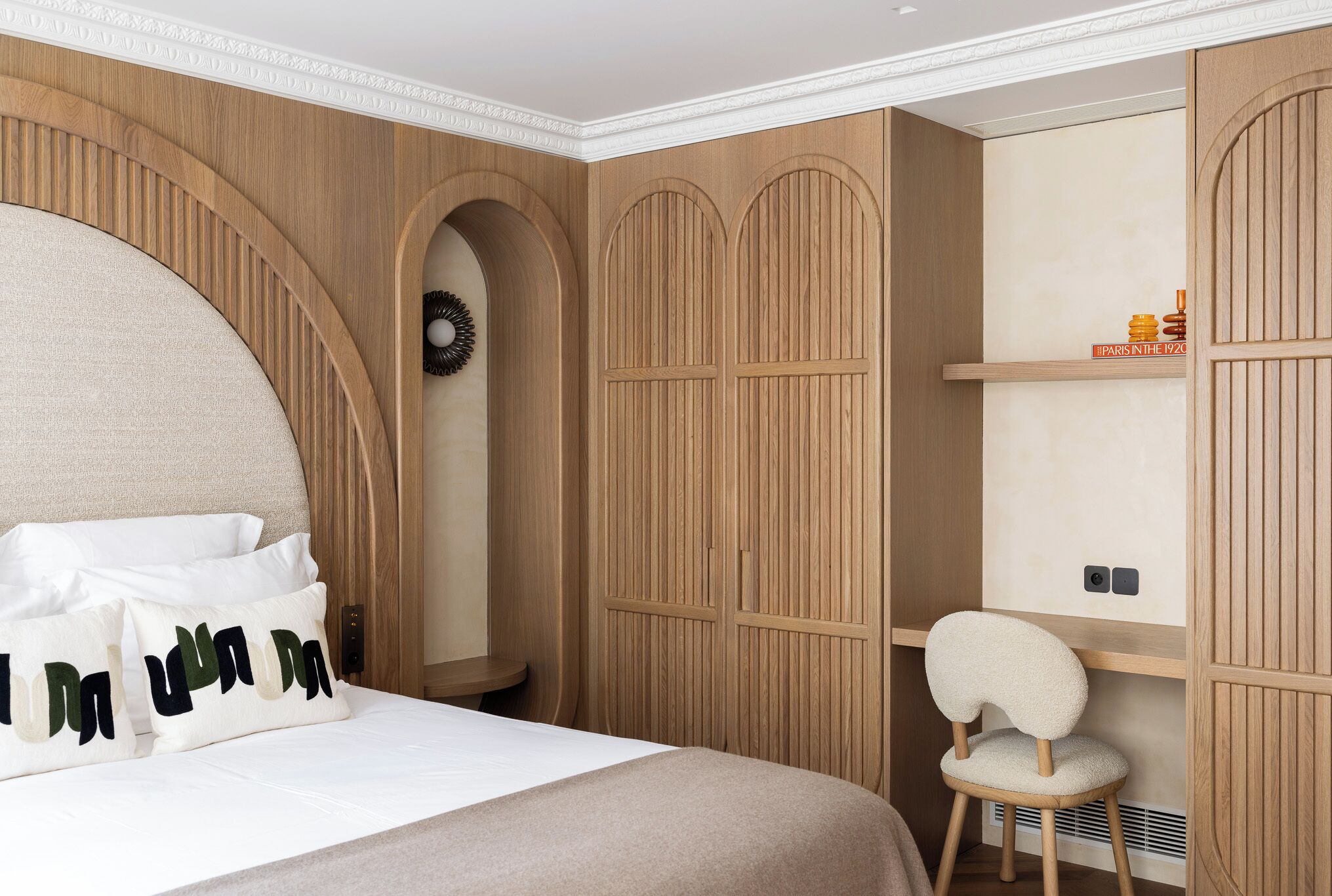 A bedroom with a large bed, wooden wardrobe, and a small chair.