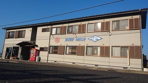 Un bâtiment à deux étages avec une enseigne indiquant « MAGASIN DE PLANCHES DE SURF » et un logo au-dessus.