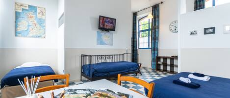 A room with two beds, a table with a book, a map, and a TV on the wall.