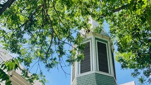 A green building with a white door and arched windows, featuring a tower with a vent. - The Downtown Abbey (San Marcos)