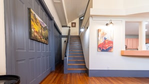 A staircase with wooden steps and a handrail, leading to a landing with a painting and a light fixture. - The Downtown Abbey (San Marcos)