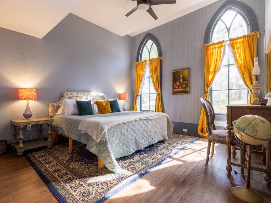A bedroom with a large bed, a globe on a stand, and a window with curtains.