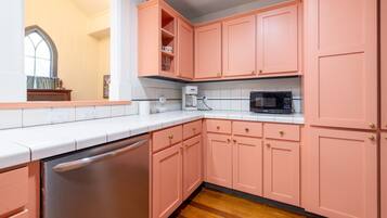 A kitchen with pink cabinets, a stainless steel dishwasher, a microwave, and a coffee maker.