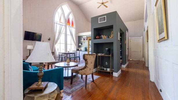 A spacious living room with a high ceiling, a large window, a television, a dining table, and a bookshelf. - The Downtown Abbey (San Marcos)