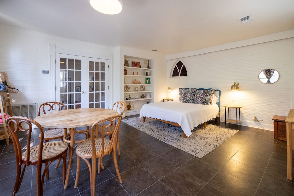 A room with a bed, bedside table, lamp, and a bookshelf.