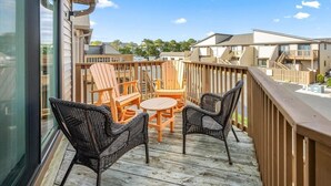 A wooden deck with outdoor furniture, a glass door, and a view of neighboring buildings.