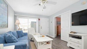 A room with a blue sofa, a white coffee table, a white TV stand, and a ceiling fan.