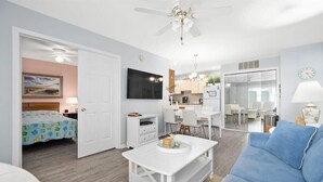 A modern living room with a sofa, a coffee table, a TV, and a dining area with chairs and a table.