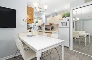 A modern kitchen with white cabinets, a central island, and a dining area with a white table and chairs.