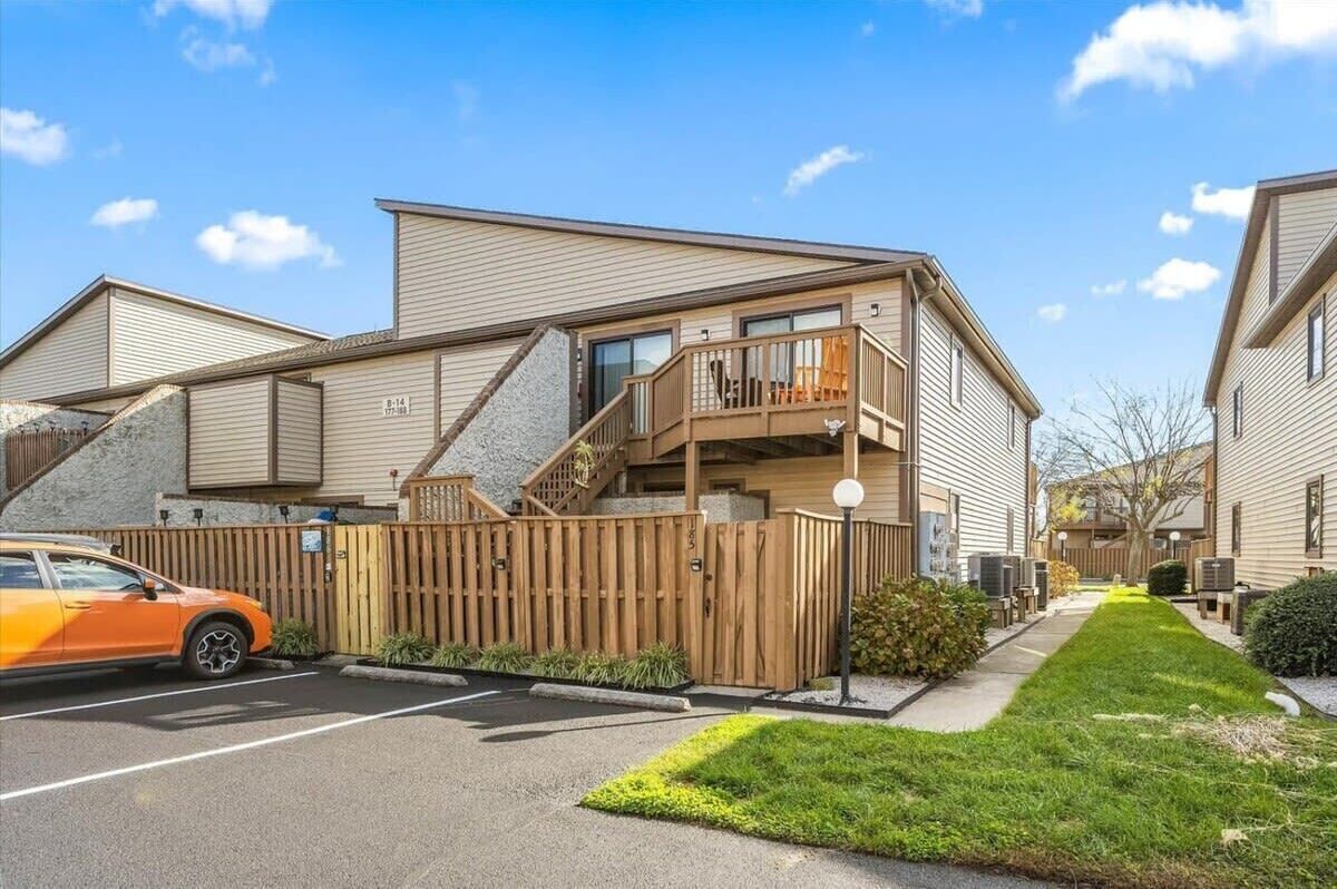 A residential building with a balcony, a staircase, and a fenced driveway.
