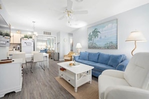 A modern living room with a white sofa, a coffee table, and a dining area with white furniture.