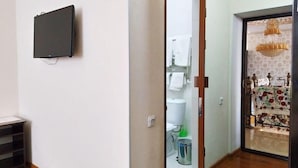 A hotel room with a television mounted on the wall, a wooden floor, a door leading to a bathroom with a toilet and sink, and a patterned curtain. - Euro-asia (Khiva)