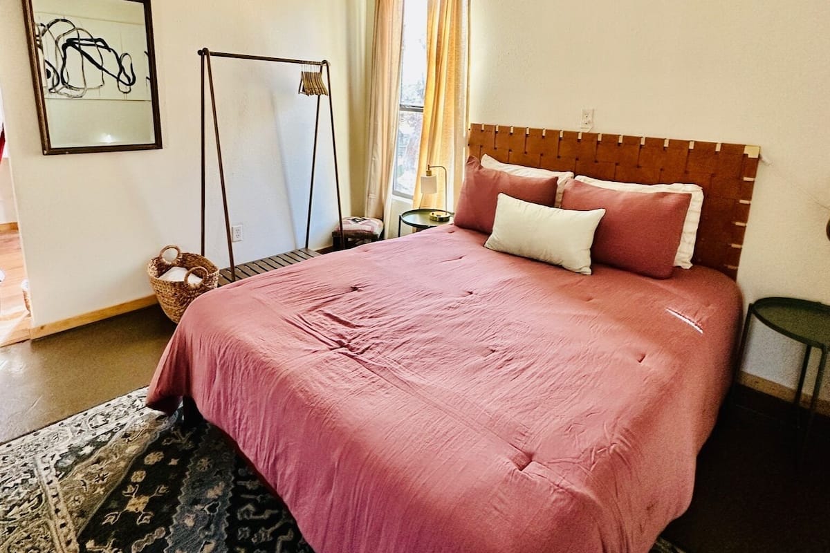 A bedroom with a large bed, a ceiling fan, a window with curtains, a bedside table, and a rug.