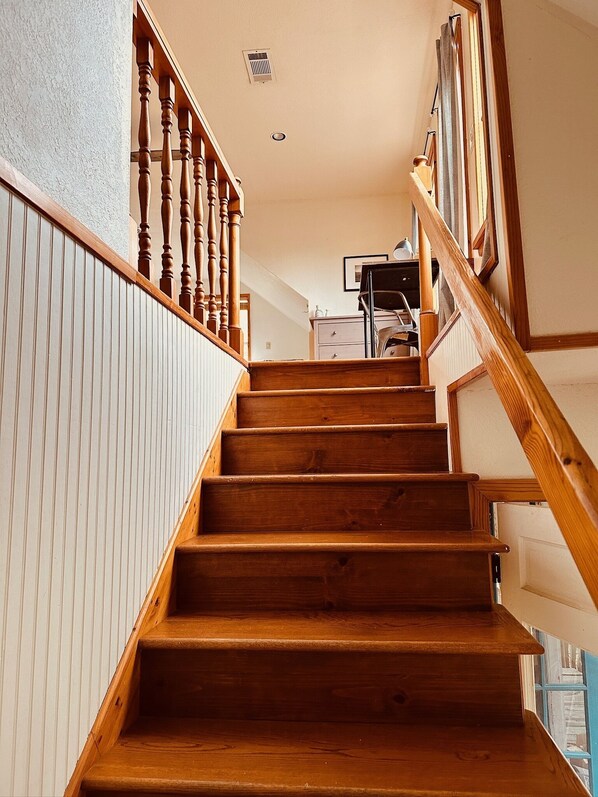 A wooden staircase with a handrail, leading to a landing with a white radiator and a framed picture on the wall. - Mosaic On The Hill (San Marcos)