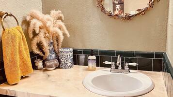 A bathroom with a beige countertop, a white sink, a gold-framed mirror, and a yellow towel.