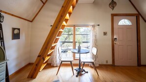 A room with a sloped ceiling, a wooden staircase, a round table with chairs, a door with a window, and a hanging light fixture.