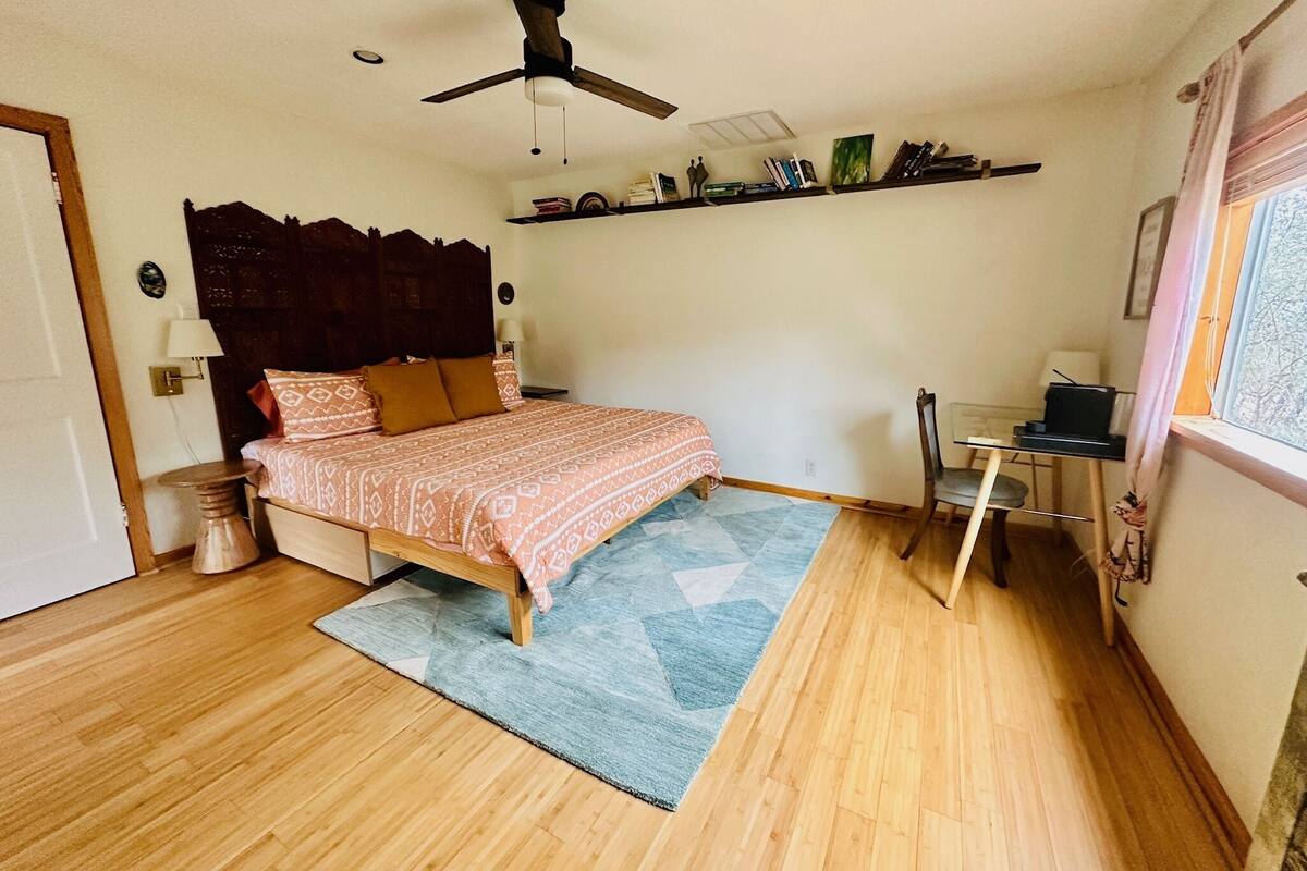 A bedroom with a bed, a desk, a chair, a ceiling fan, a window, and a bookshelf.