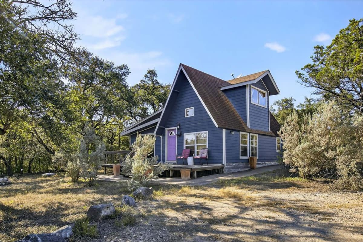 A two-story house with a sloped roof, a front porch with seating, and a small deck area.