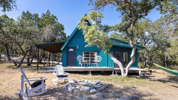 A blue cabin with a porch, surrounded by trees, and a hammock.