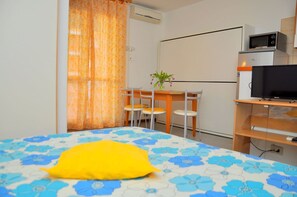 Une chambre avec un lit, un bureau, une chaise, une télévision et un four à micro-ondes.